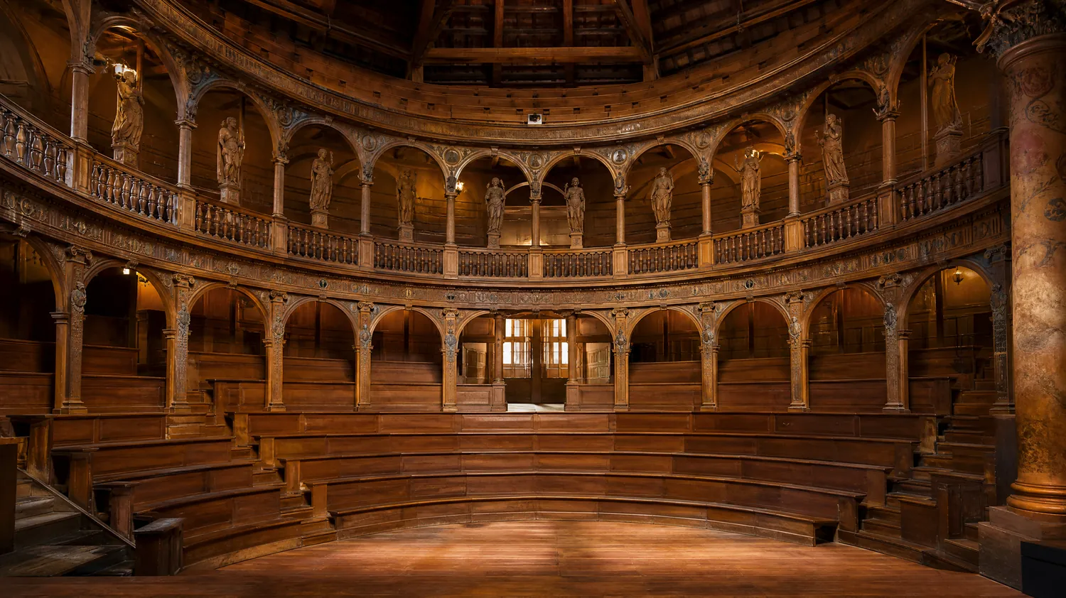 The interior of the wooden Teatro Farnese with curved tiers, arched galleries and statues, lit warmly