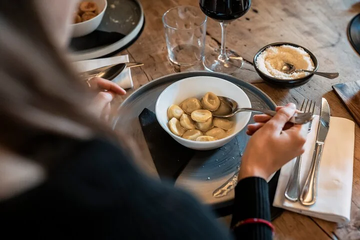A diner lifting stuffed pasta from a bowl, with a glass of red wine on the table