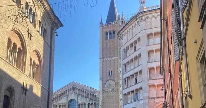 A bright view from a side street of the Parma Baptistery's loggias, the brick bell tower and the top of the cathedral facade