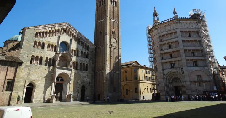 The Parma cathedral facade, bell tower and octagonal Baptistery across a sunny square, with visitors queuing along the side