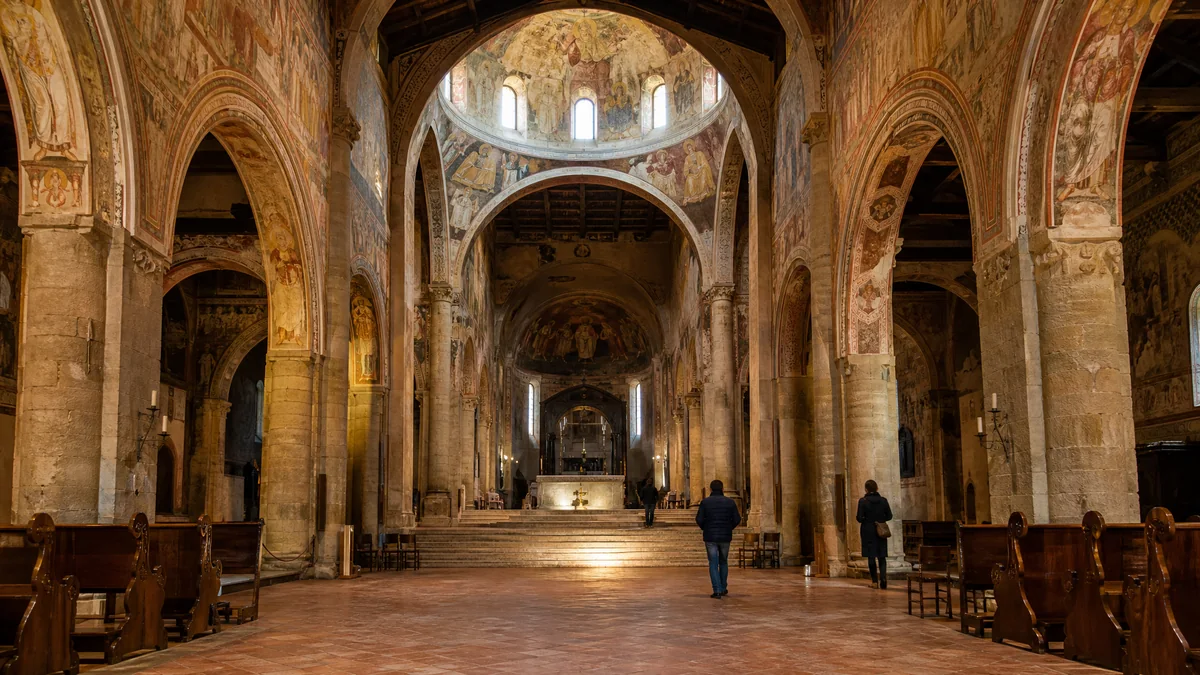 La nef d'une cathédrale romane aux murs couverts de fresques, avec la lumière tombant de la coupole à la croisée